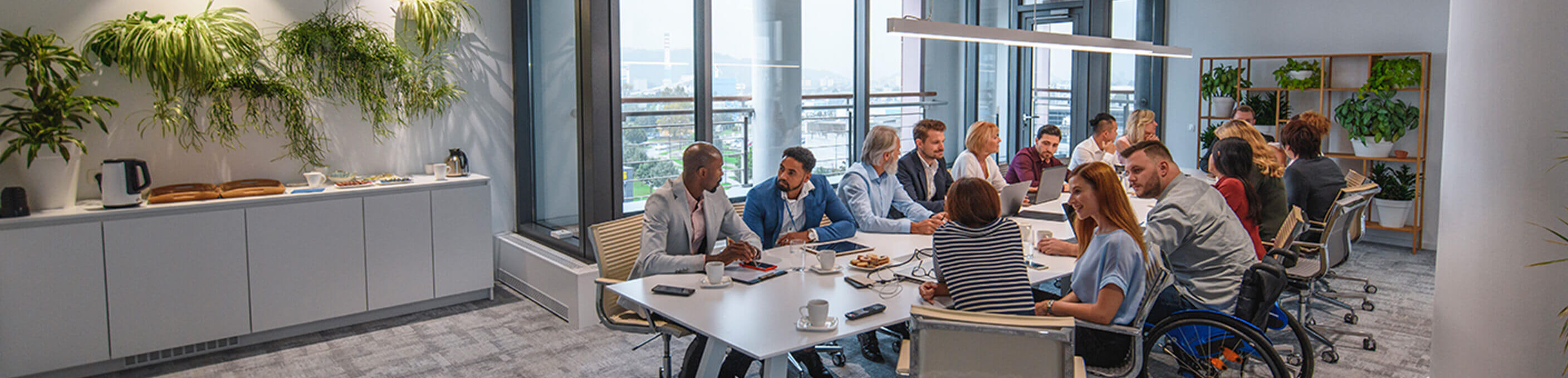 A business conference room with a large group of diverse professionals seated at a long table. 