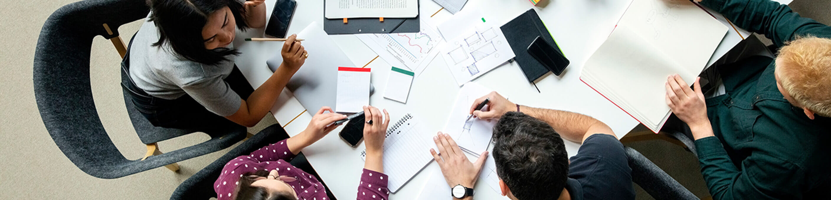 A group of four ethnically diverse business people working together on documents at a table. 