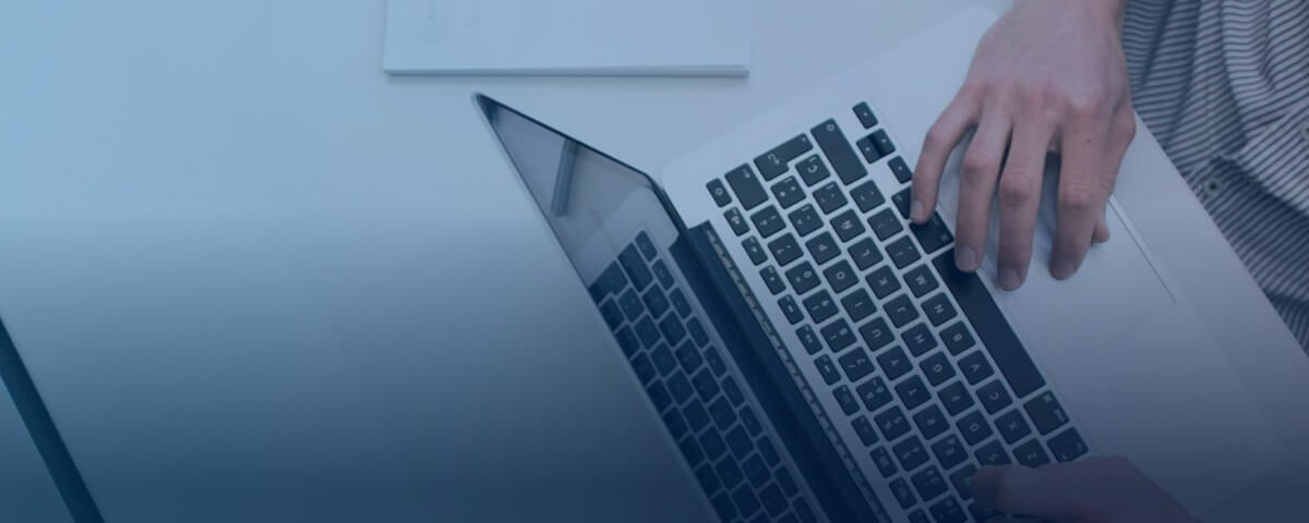 A Caucasian man seated at a desk typing on a laptop keyboard. 