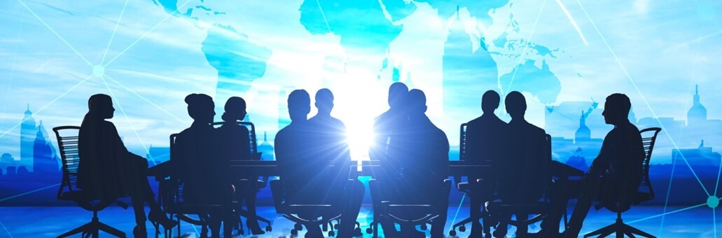 Silhouette of a group of businesspeople seated at a table against a modern blue globe background.