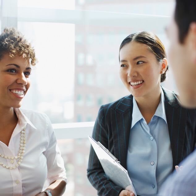 Three businesspeople smiling and talking in an office.