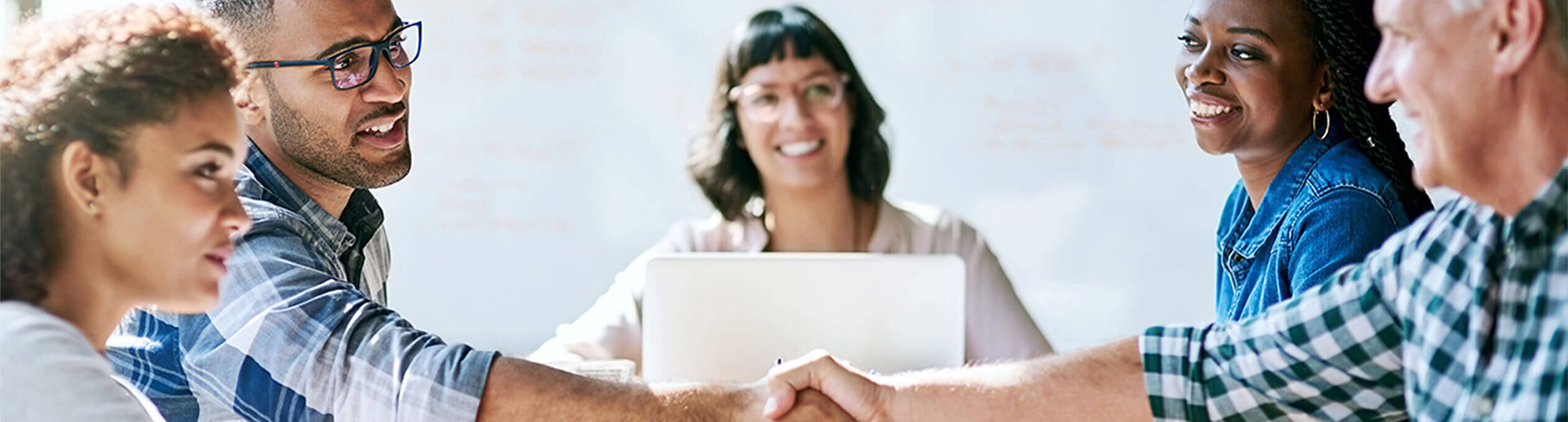 A group of business people around a table, shaking hands.