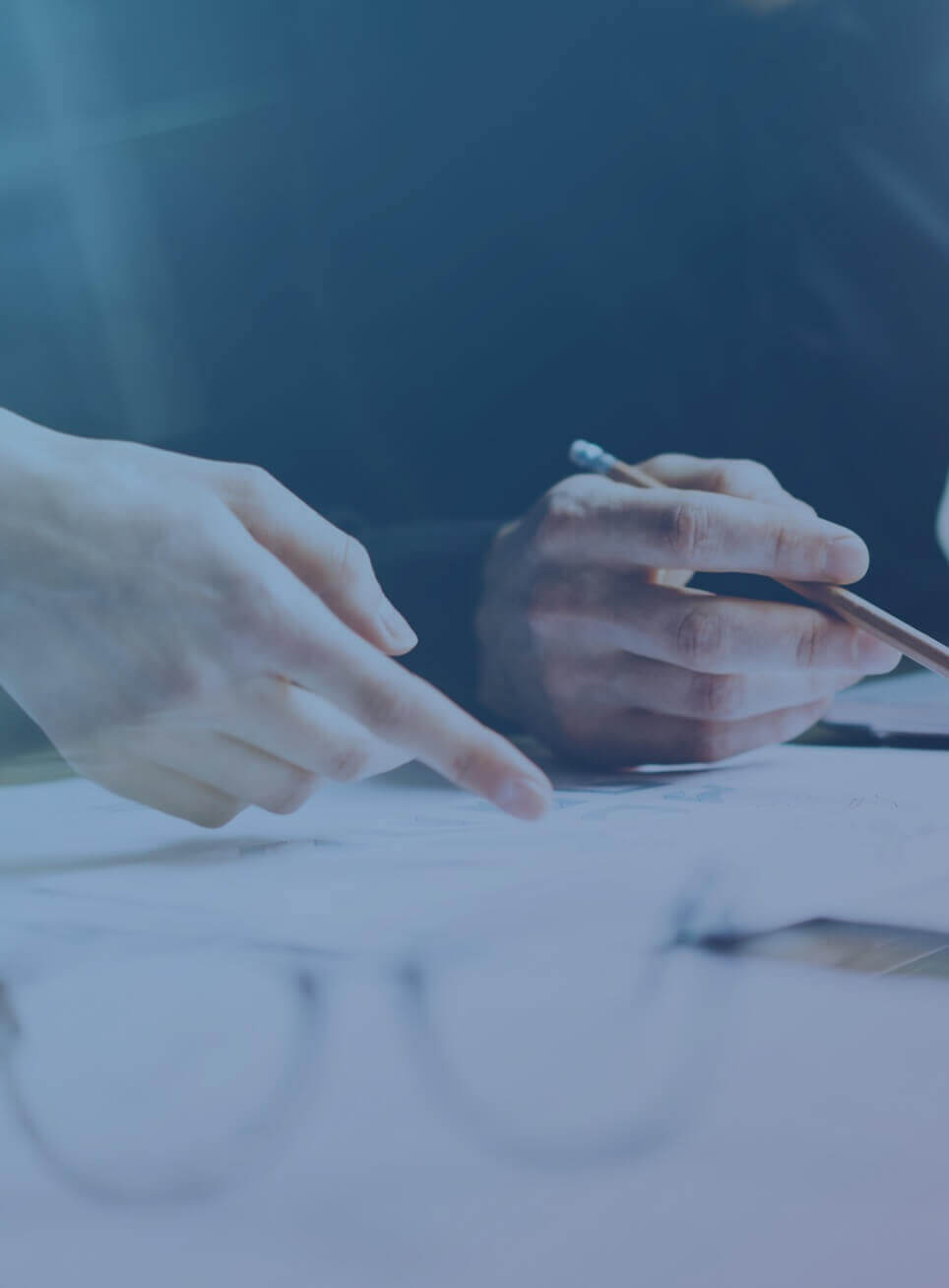 Two people's hands with documents, a pen, and eyeglasses on a table. 