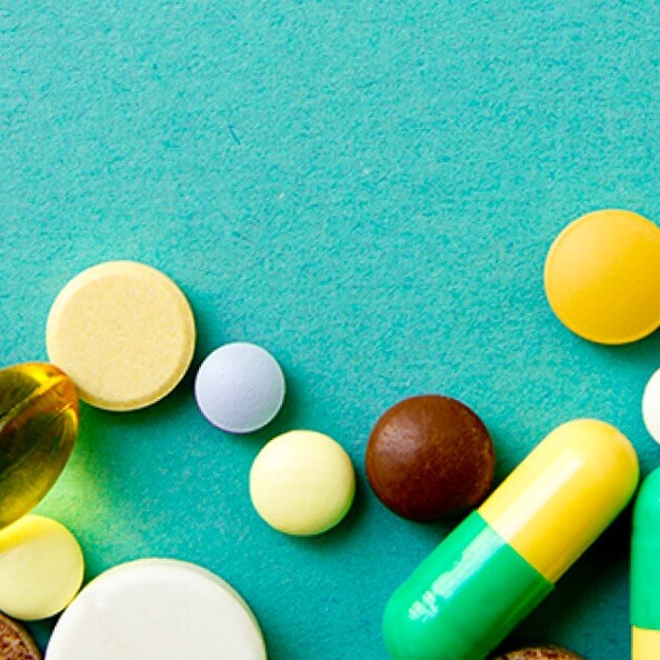 About a dozen different vitamins or supplement tablets and capsules on a teal background. 