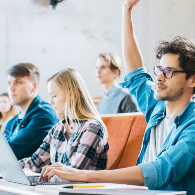 A group of university students in a lecture hall with one male raising his hand. 