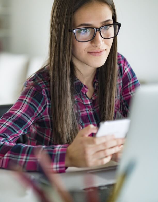 A long-haired yound woman in a pink plaid shirt looking at her cell phone. 