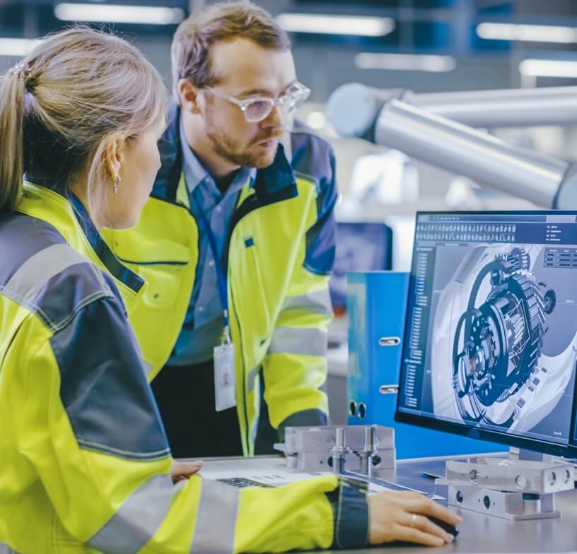 A male and female engineer in bright yellow safety jackets looking at a computer screen together. 