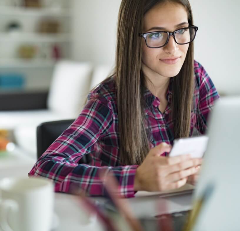 A young woman with long brown hair land glasses ooking at a cellphone in an office. 