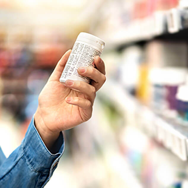 A woman's arm and her hand holding a bottle of vitamins in a store. 