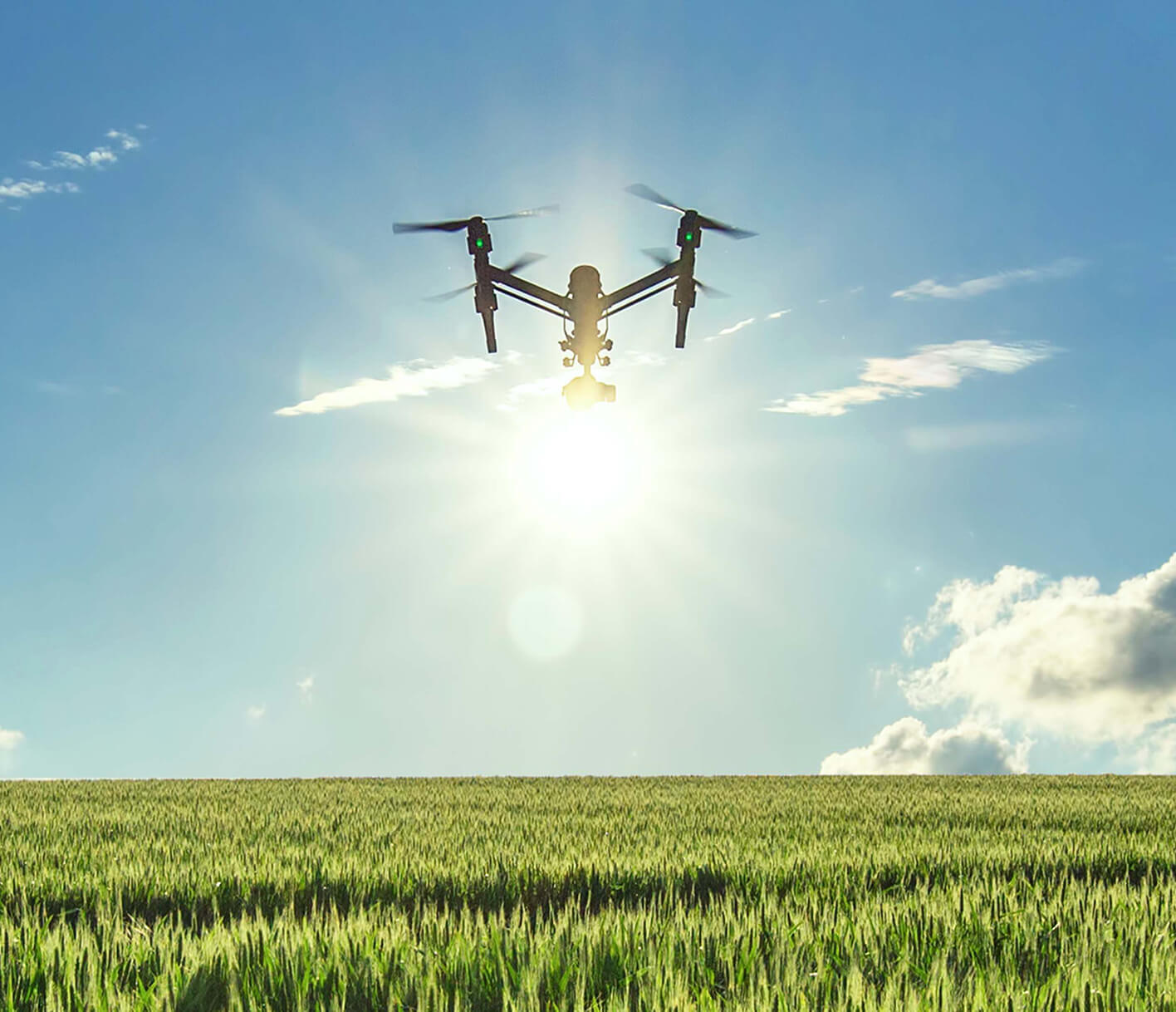 Drone flying over a field in the sun.