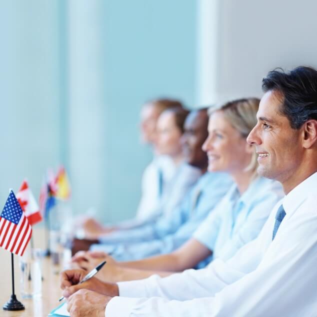 Five people seated at a conference table with small multinational flags in front of them. 