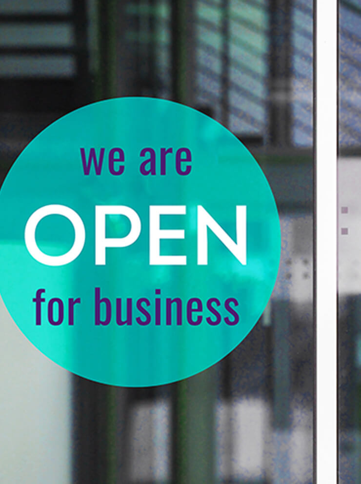 A teal sign in the window of a business announcing it's open.