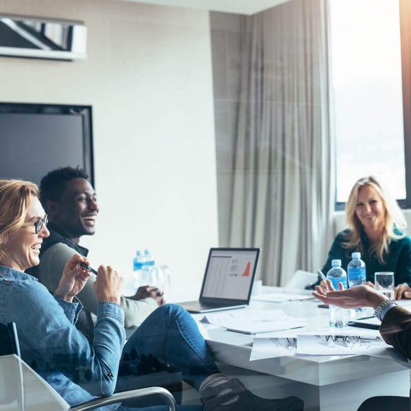 A small group of smiling people talking and working together in a meeting room with tablet computers and bottles of water.