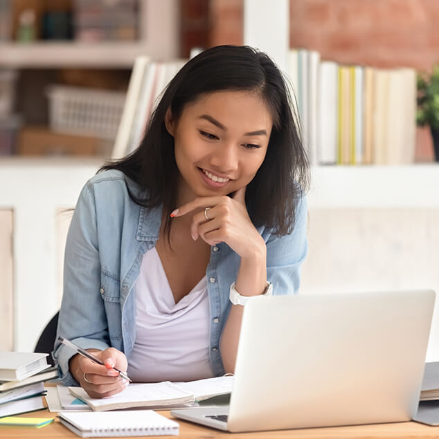 A female college student smiling as she works on a laptop.