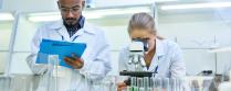 Two laboratory workers with a clipboard and microscope in an environmental lab. 