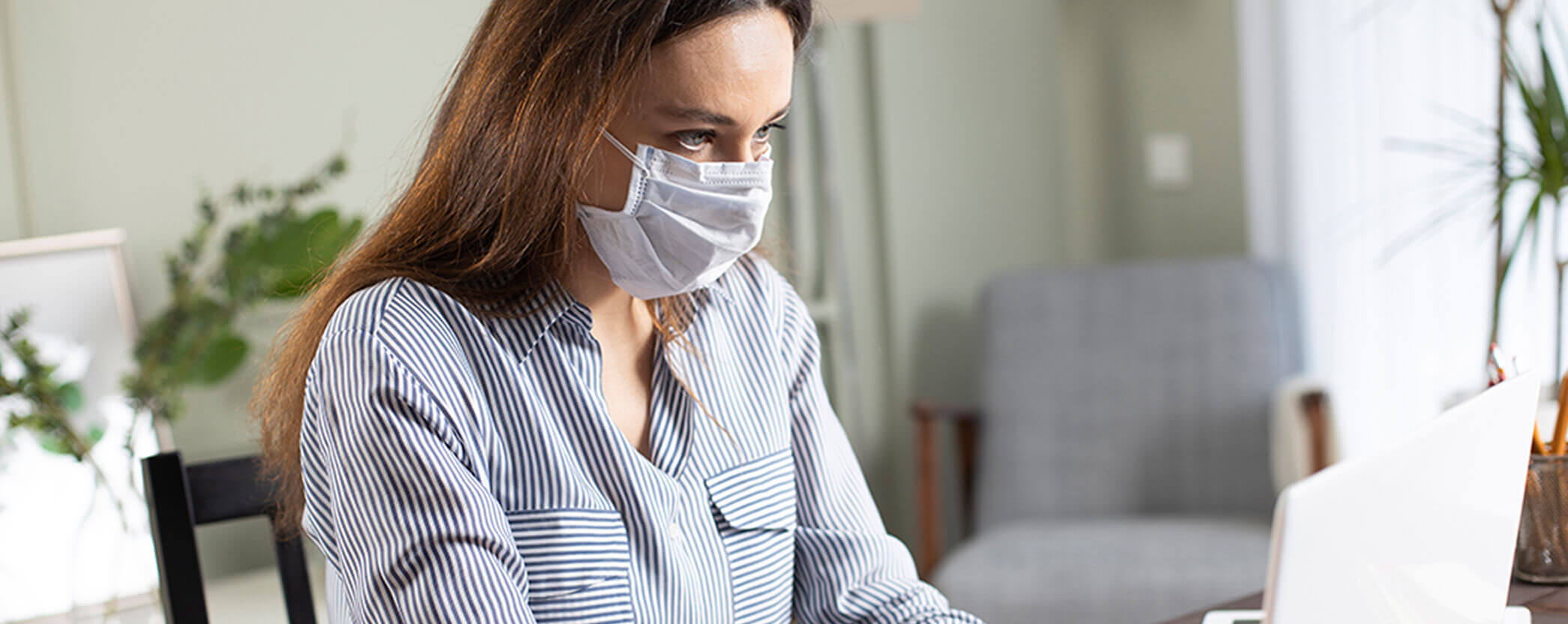 A female office worker wears a mask as she looks at her computer screen.