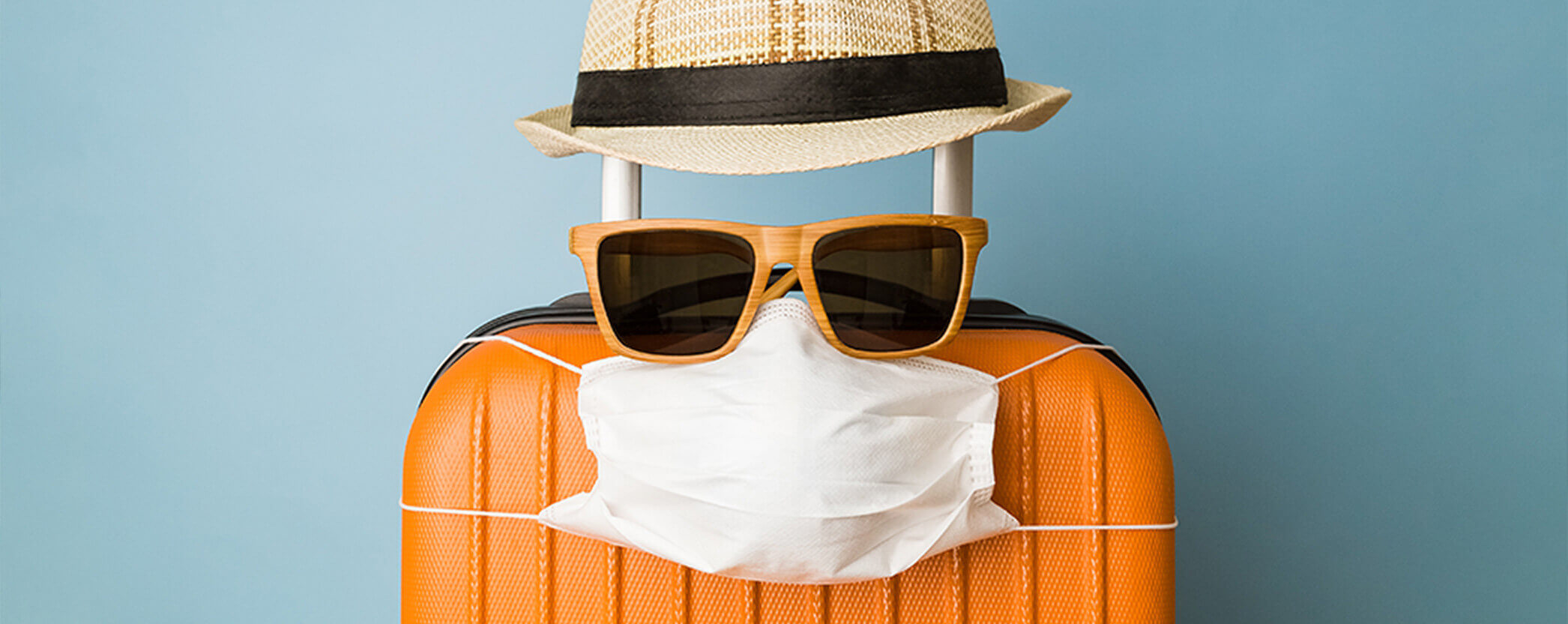 A suitcase with a PPE face mask, sunglasses, and a hat.